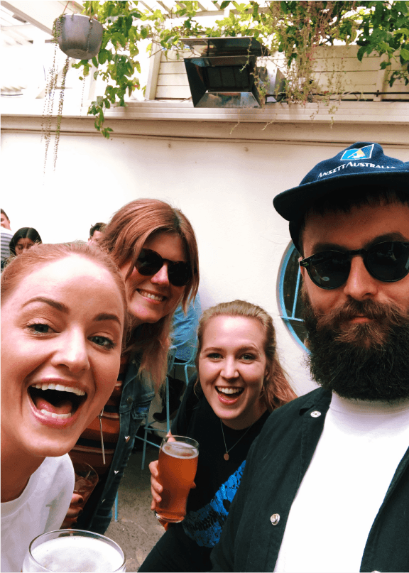 A selfie of four team members, two of whom are holding beers. All four are smiling at the camera