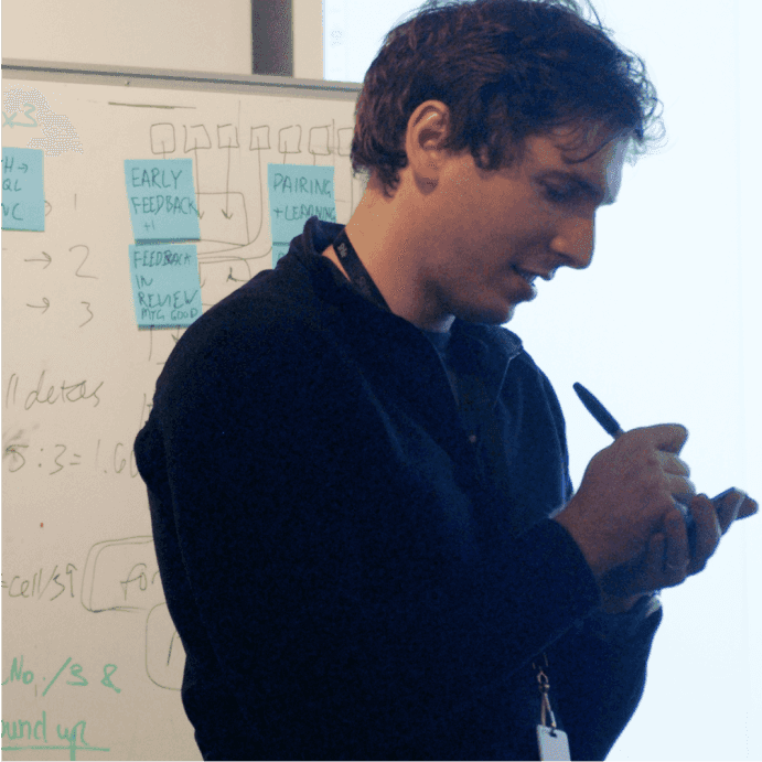 An engineer stands in front of a whiteboard, writing onto a notepad in his hand
