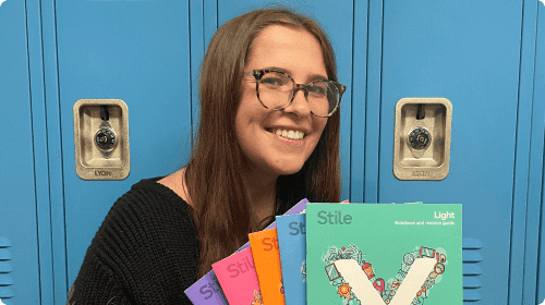 A headshot of Alex holding several Stile X booklets and smiling at the camera, in front of blue school lockers