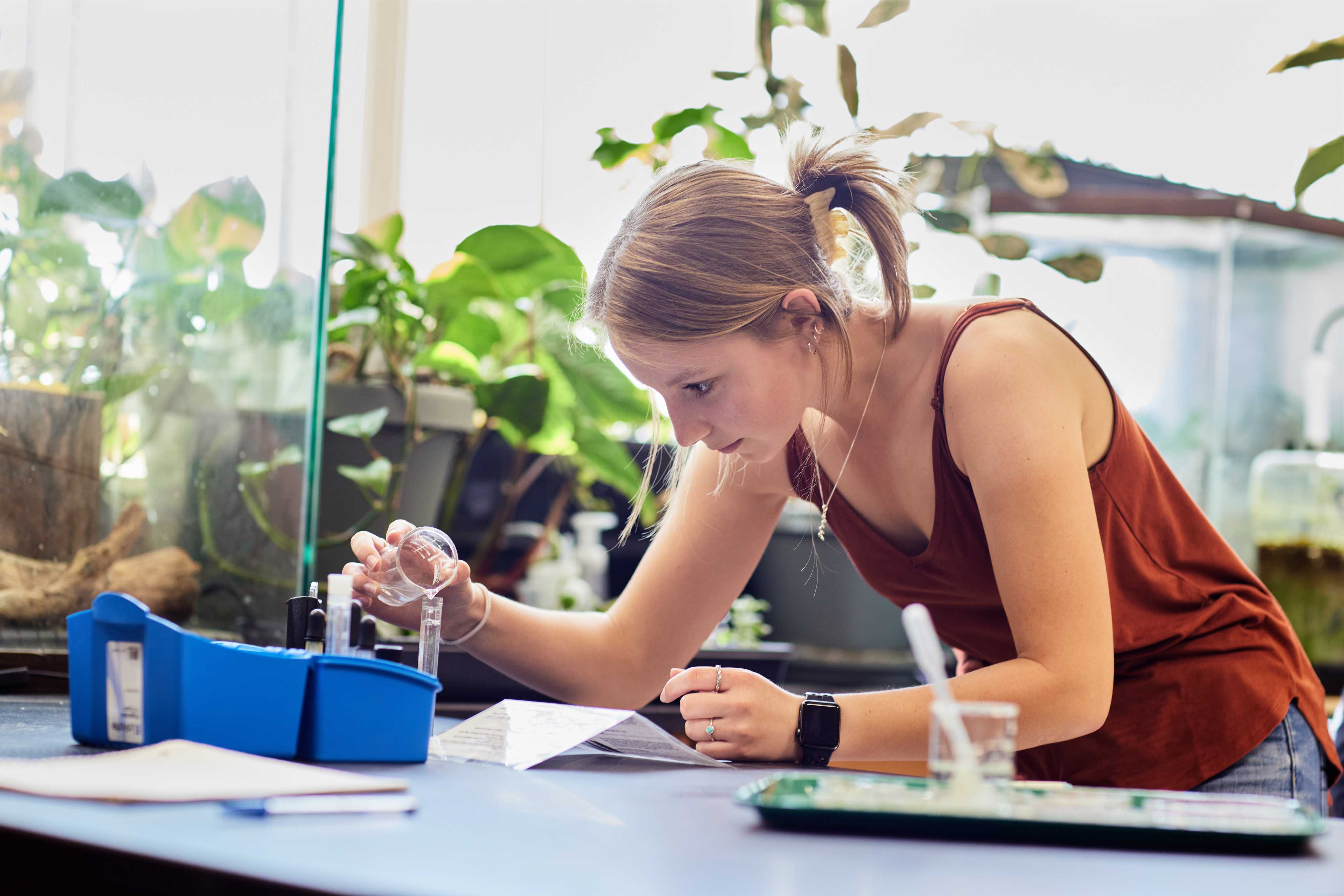 A student in a science classroom pouring liquid from a beaker into a test tube during an experiment.