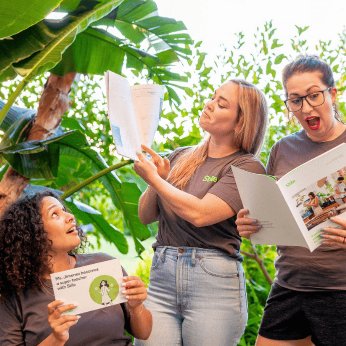 Three Stile staff posing with our teacher materials, with plants in the background