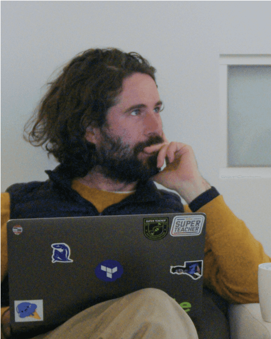 An engineer is sitting with a laptop on his lap, looking thoughtful at something off camera