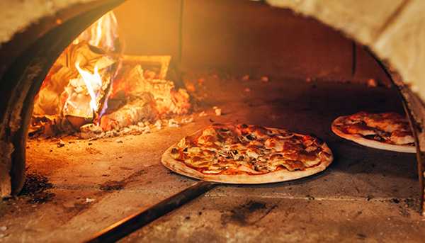 The inside of a pizza oven, with fire and two pizzas cooking inside