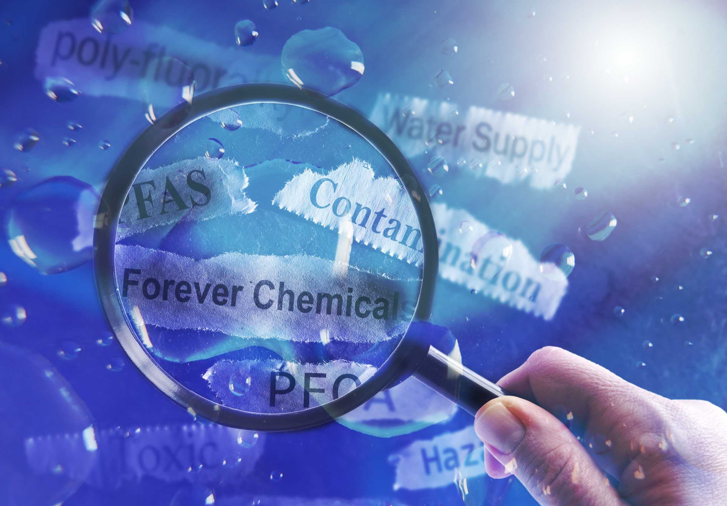 A hand holding a magnifying glass over torn paper labels reading 'Forever Chemicals', 'PFAS' and 'Contamination' in water.