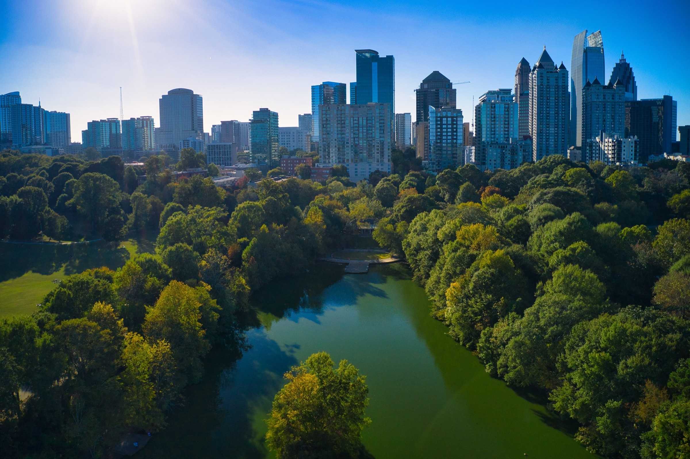 Aerial view of the Atlanta skyline rising above a green tree canopy and a park lake.
