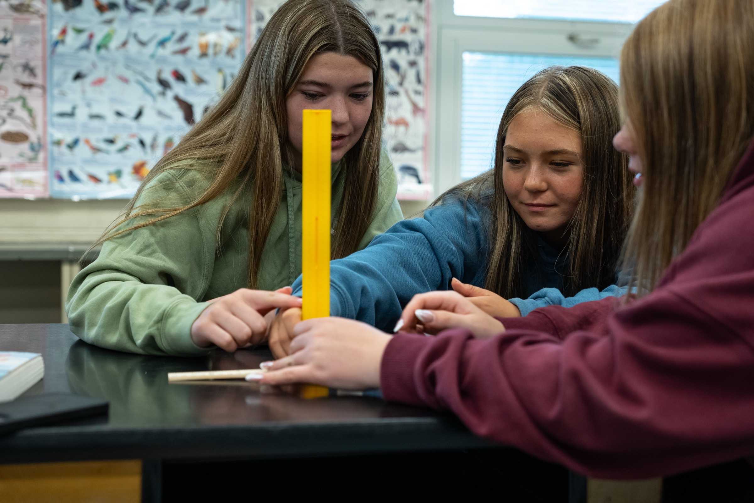 Three students collaborating on a science activity at a lab bench.