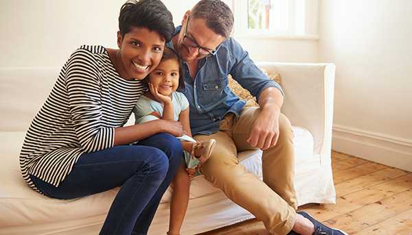 A family is shown sitting together on a couch and smiling